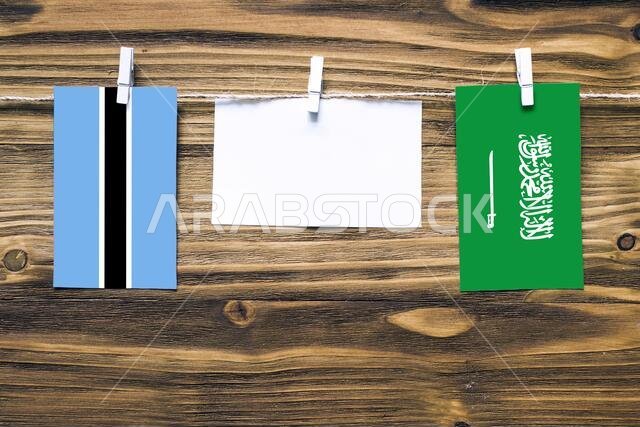 أعلام بوتسوانا والمملكة العربية السعودية معلقة بحبل بمشابك غسيل، مع مساحة للكتابة على ورقة بيضاء على خلفية خشبية. علاقات دبلوماسية