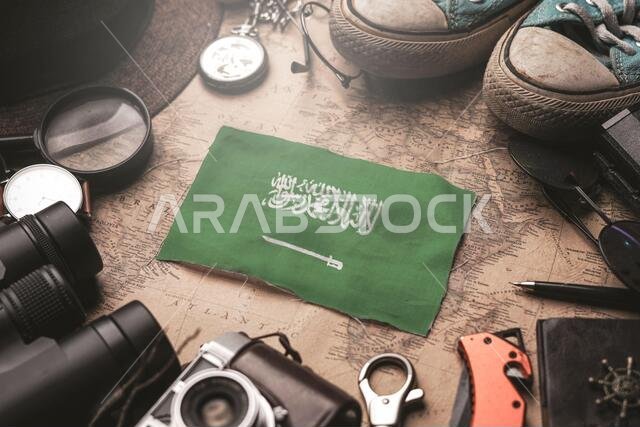 علم المملكة العربية السعودية بين أغراض المسافر على خريطة قديمة. مفهوم الوجهة السياحية.