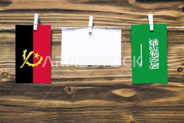أعلام أنغولا والسعودية معلقة بحبل بمشابك غسيل، مع مساحة للكتابة على ورقة بيضاء على خلفية خشبية. العلاقات الدبلوماسية