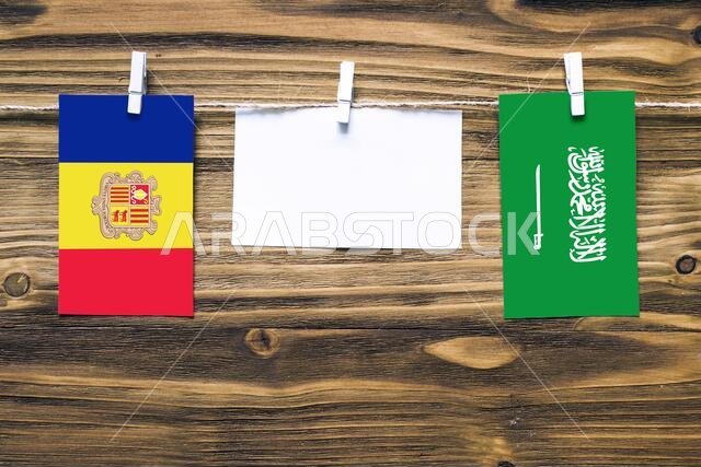 أعلام أندورا والمملكة العربية السعودية معلقة بحبل بمشابك غسيل، مع مساحة للكتابة على ورقة بيضاء على خلفية خشبية. علاقات دبلوماسية