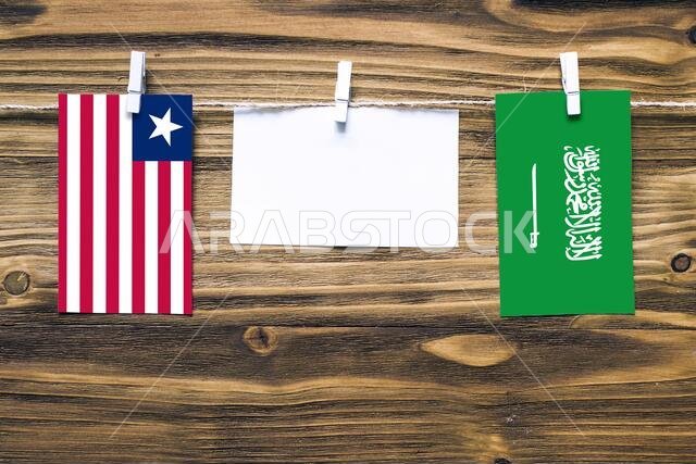 Hanging flags of Liberia and Saudi Arabia attached to rope with clothes pins with copy space on white note paper on wooden background.Diplomatic relat