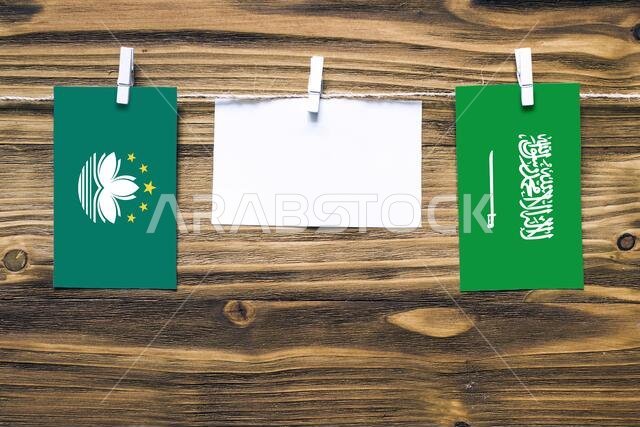 Hanging flags of Macao and Saudi Arabia attached to rope with clothes pins with copy space on white note paper on wooden background.Diplomatic relatio