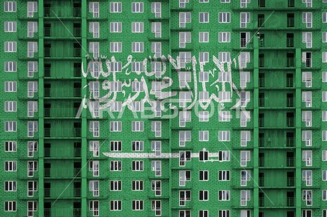 Saudi Arabia flag depicted in paint colors on multi-storey residental building under construction. Textured banner on big brick wall background