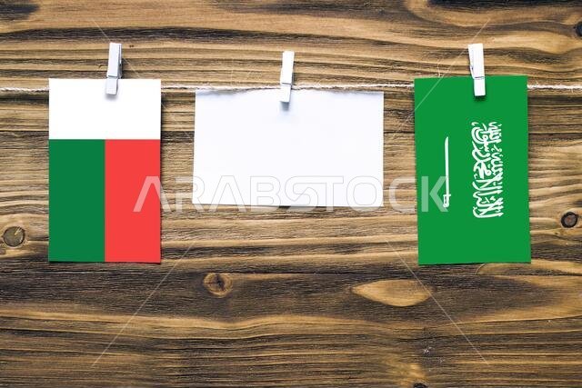 Hanging flags of Madagascar and Saudi Arabia attached to rope with clothes pins with copy space on white note paper on wooden background.Diplomatic re