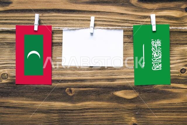 Hanging flags of Maldives and Saudi Arabia attached to rope with clothes pins with copy space on white note paper on wooden background.Diplomatic rela