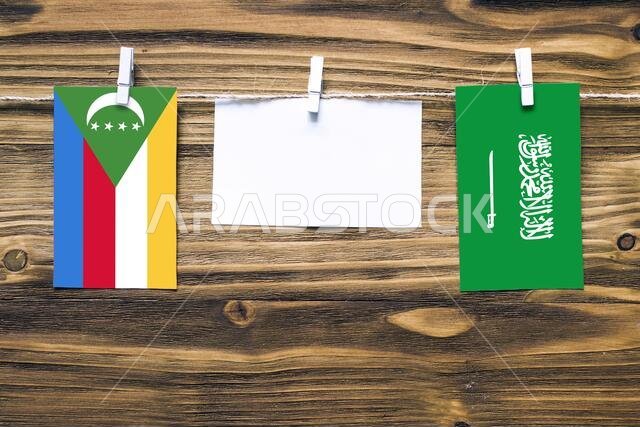 أعلام جزر القمر والمملكة العربية السعودية معلقة بحبل بمشابك غسيل، مع مساحة للكتابة على ورقة بيضاء على خلفية خشبية. علاقات دبلوماسية