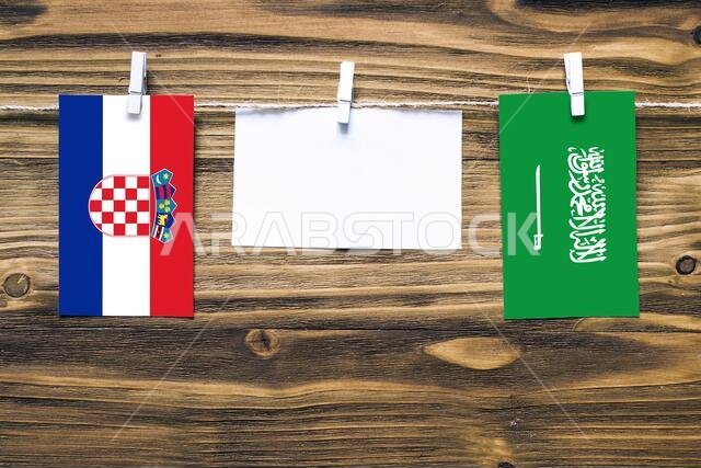 Hanging flags of Croatia and Saudi Arabia attached to rope with clothes pins with copy space on white note paper on wooden background.Diplomatic relat
