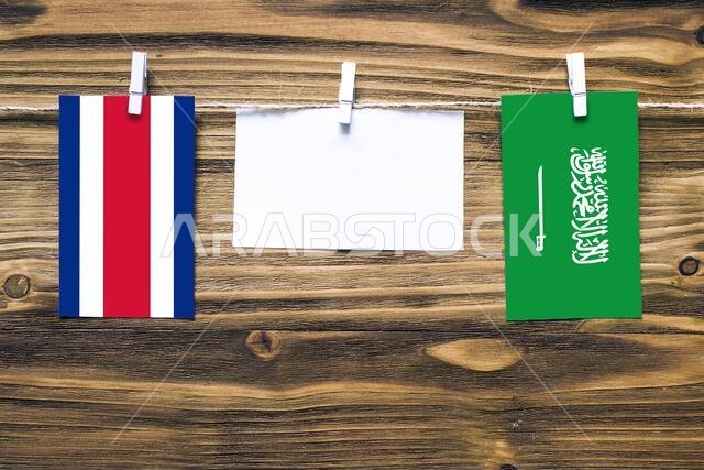 Hanging flags of Costa Rica and Saudi Arabia attached to rope with clothes pins with copy space on white note paper on wooden background.Diplomatic re