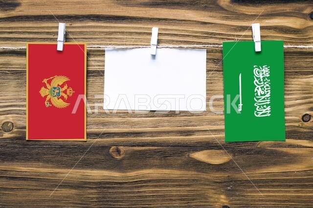 Hanging flags of Montenegro and Saudi Arabia attached to rope with clothes pins with copy space on white note paper on wooden background.Diplomatic re