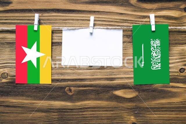 Hanging flags of Myanmar and Saudi Arabia attached to rope with clothes pins with copy space on white note paper on wooden background.Diplomatic relat