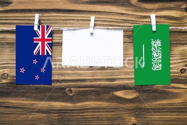 Hanging flags of New Zealand and Saudi Arabia attached to rope with clothes pins with copy space on white note paper on wooden background.Diplomatic r