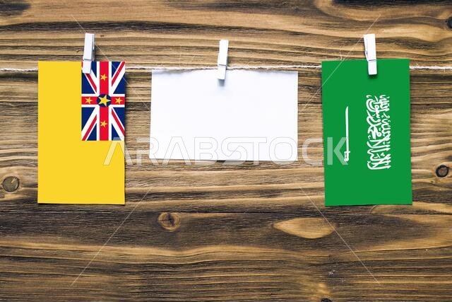 Hanging flags of Niue and Saudi Arabia attached to rope with clothes pins with copy space on white note paper on wooden background.Diplomatic relation