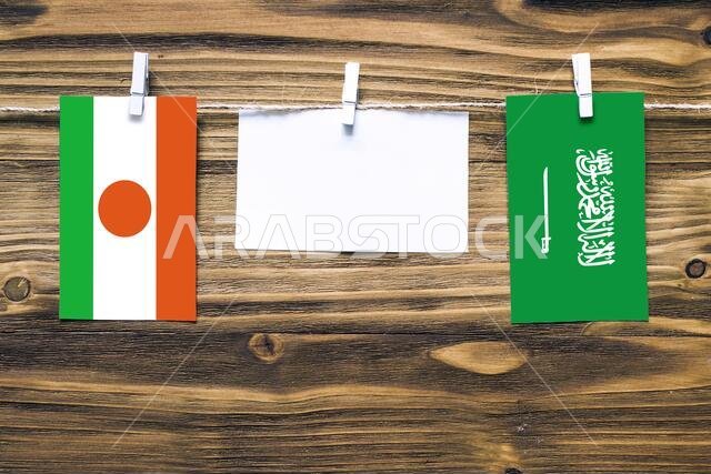 Hanging flags of Niger and Saudi Arabia attached to rope with clothes pins with copy space on white note paper on wooden background.Diplomatic relatio