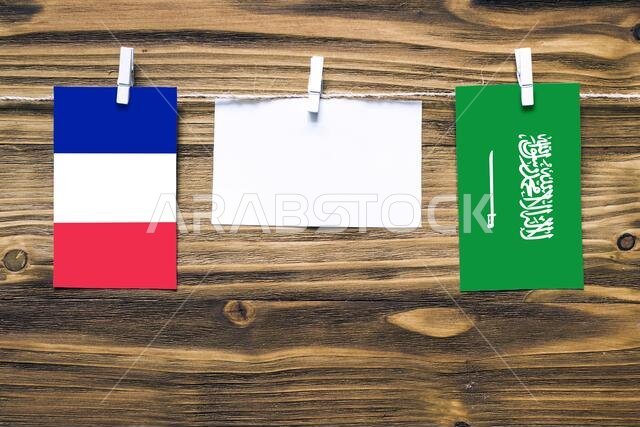 Hanging flags of France and Saudi Arabia attached to rope with clothes pins with copy space on white note paper on wooden background.Diplomatic relati