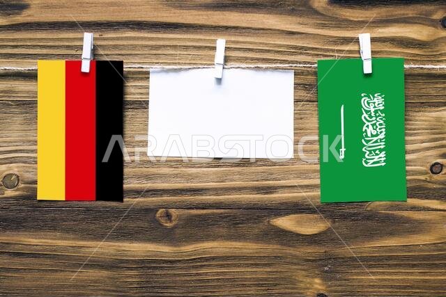 Hanging flags of Germany and Saudi Arabia attached to rope with clothes pins with copy space on white note paper on wooden background.Diplomatic relat