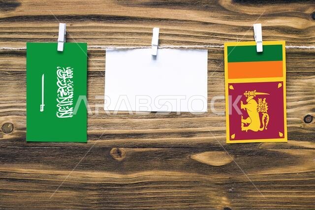 Hanging flags of Saudi Arabia and Sri Lanka attached to rope with clothes pins with copy space on white note paper on wooden background.Diplomatic rel