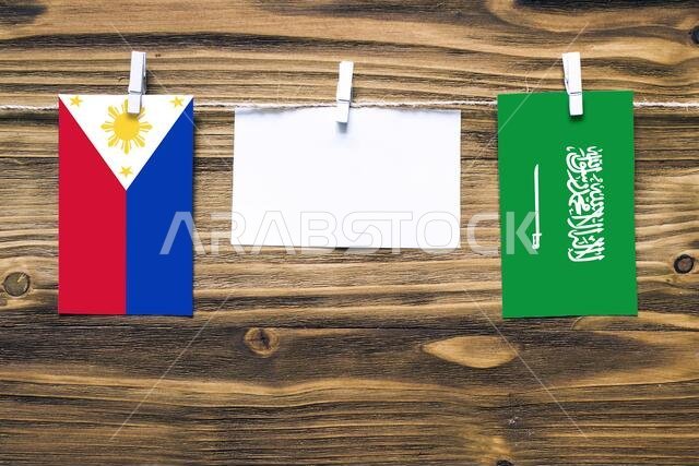Hanging flags of Philippines and Saudi Arabia attached to rope with clothes pins with copy space on white note paper on wooden background.Diplomatic r