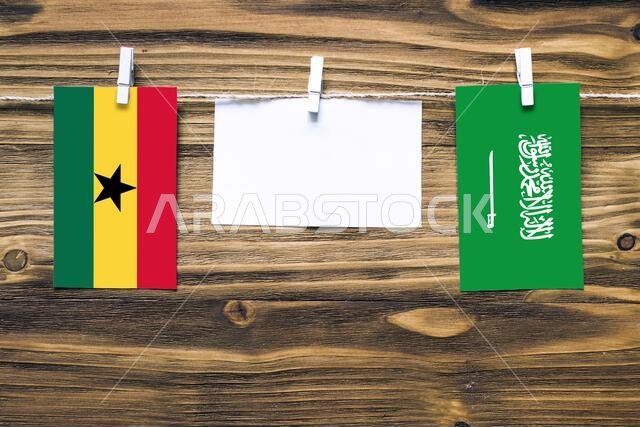 Hanging flags of Ghana and Saudi Arabia attached to rope with clothes pins with copy space on white note paper on wooden background.Diplomatic relatio
