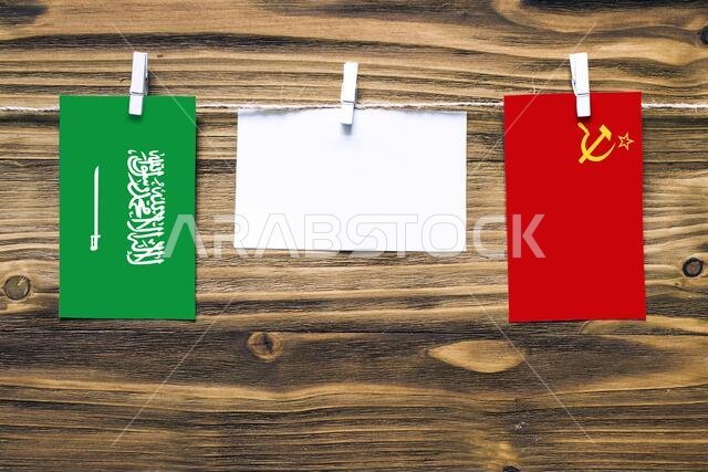Hanging flags of Saudi Arabia and Soviet Union attached to rope with clothes pins with copy space on white note paper on wooden background.Diplomatic