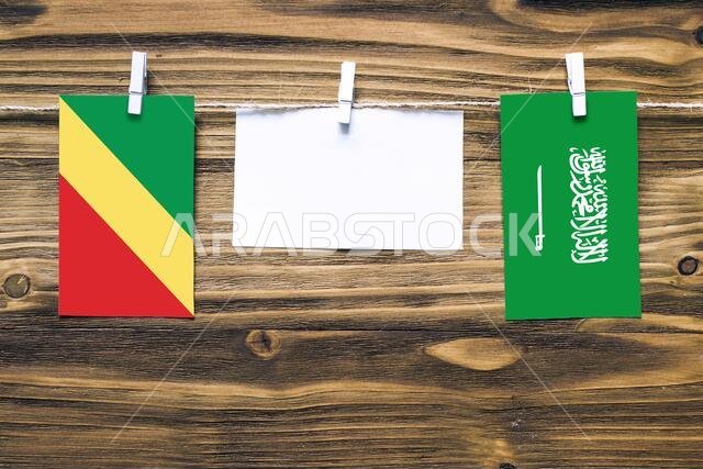 Hanging flags of Republic Of The Congo and Saudi Arabia attached to rope with clothes pins with copy space on white note paper on wooden background.Di
