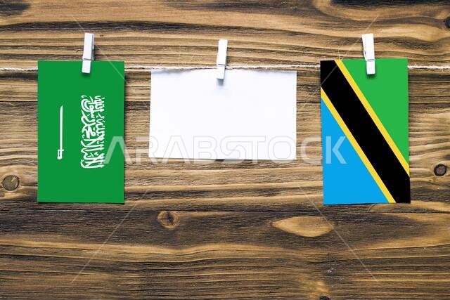 Hanging flags of Saudi Arabia and Tanzania attached to rope with clothes pins with copy space on white note paper on wooden background.Diplomatic rela