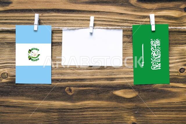 Hanging flags of Guatemala and Saudi Arabia attached to rope with clothes pins with copy space on white note paper on wooden background.Diplomatic rel