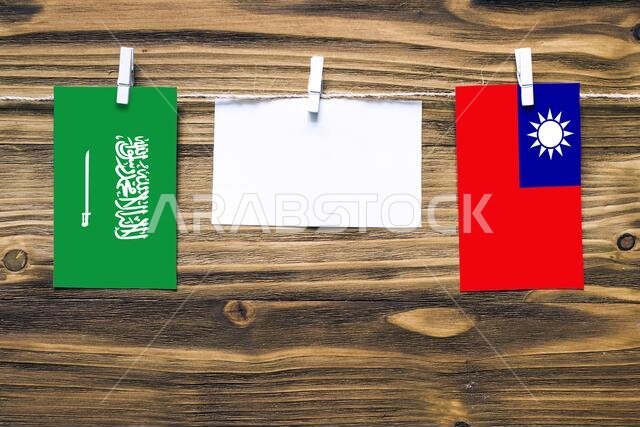 Hanging flags of Saudi Arabia and Taiwan attached to rope with clothes pins with copy space on white note paper on wooden background.Diplomatic relati