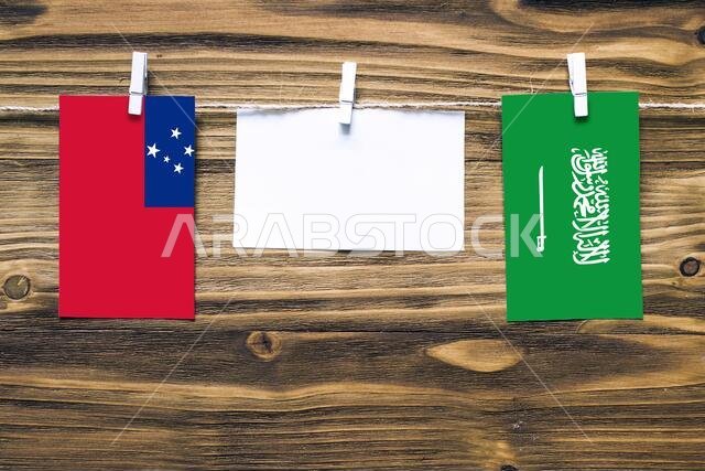 Hanging flags of Samoa and Saudi Arabia attached to rope with clothes pins with copy space on white note paper on wooden background.Diplomatic relatio