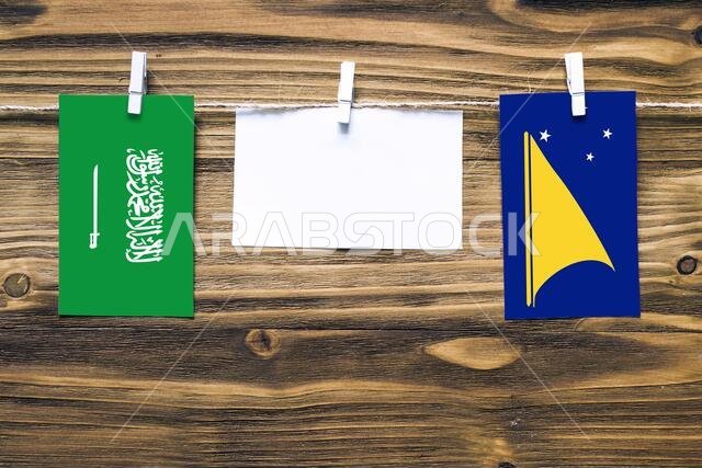 Hanging flags of Saudi Arabia and Tokelau attached to rope with clothes pins with copy space on white note paper on wooden background.Diplomatic relat
