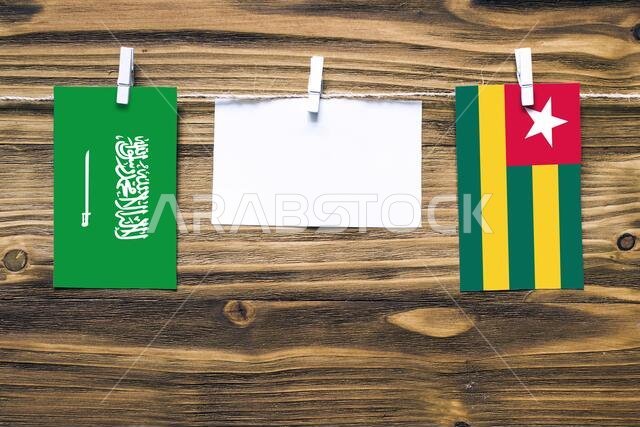 Hanging flags of Saudi Arabia and Togo attached to rope with clothes pins with copy space on white note paper on wooden background.Diplomatic relation