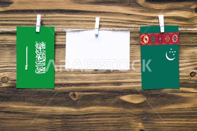 Hanging flags of Saudi Arabia and Turkmenistan attached to rope with clothes pins with copy space on white note paper on wooden background.Diplomatic