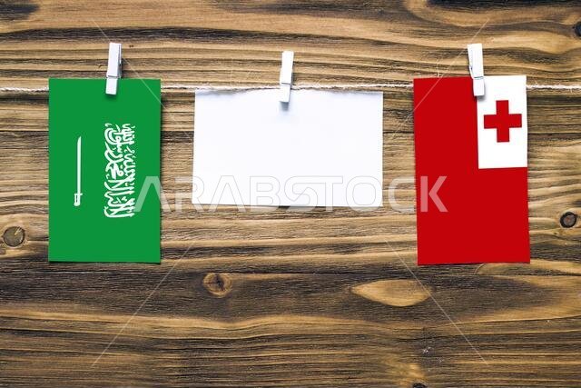 Hanging flags of Saudi Arabia and Tonga attached to rope with clothes pins with copy space on white note paper on wooden background.Diplomatic relatio