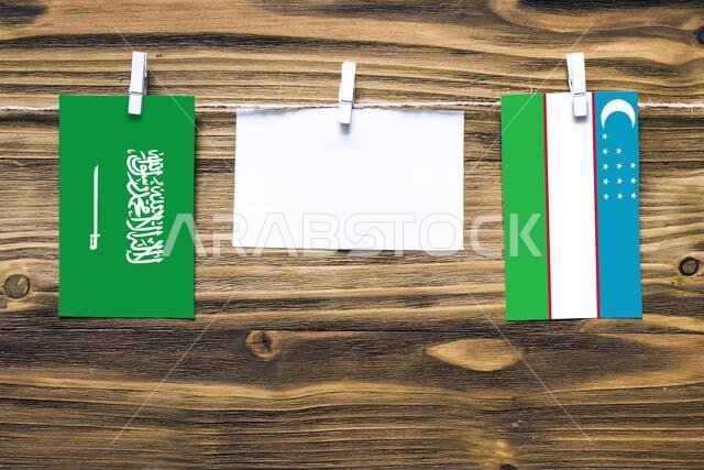 Hanging flags of Saudi Arabia and Uzbekistan attached to rope with clothes pins with copy space on white note paper on wooden background.Diplomatic re