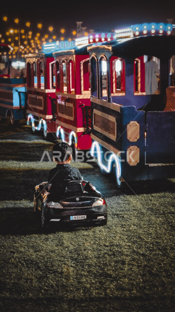 صورة لطفل صغير من الخلف يجلس على سيارة كهربائية صغيرة , نزهة في القطار , قضاء وقت ممتع , أنشطة ترفيهية , ملاهي , تسلية و ألعاب .