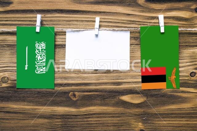 Hanging flags of Saudi Arabia and Zambia attached to rope with clothes pins with copy space on white note paper on wooden background.Diplomatic relati