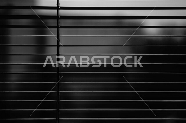 صورة باللون الأبيض والأسود لنافذة داخل منزل , ستارة رول بشرائح معدنية , غرفة مظلمة .