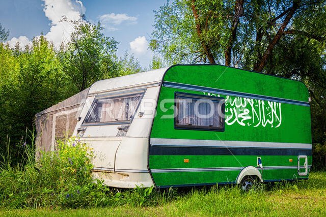 A car trailer, a motor home, painted in the national flag of  Saudi Arabia stands parked in a mountainous. The concept of road transport, trade, expor
