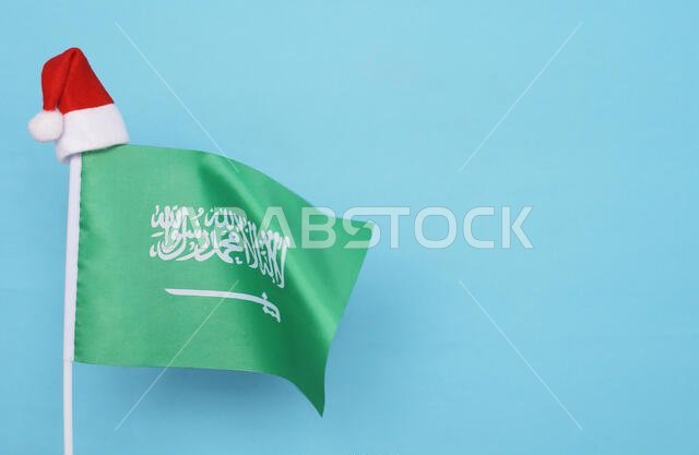 Flag of Saudi arabia with little santa claus hat on blue background. New Year winter holiday concept, copy space, beautiful