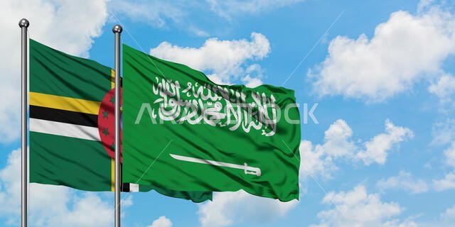 يرفرف علم دومينيكا وعلم المملكة العربية السعودية معاً في مهب الريح أمام سماء زرقاء صافية تتخللها غيوم بيضاء. مفهوم الدبلوماسية، العلاقات الدولية.