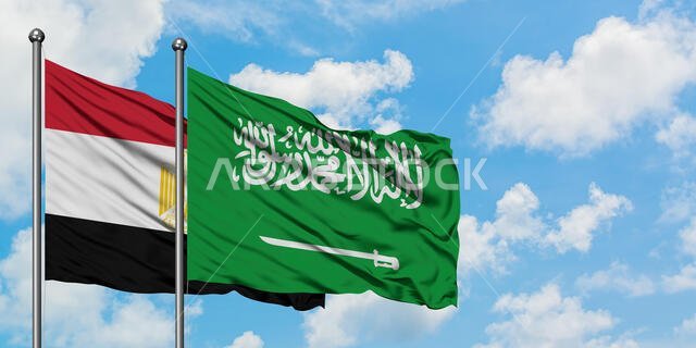 يرفرف علم مصر والسعودية معاً في مهب الريح أمام سماء زرقاء صافية تتلألأ فيها الغيوم البيضاء. مفهوم الدبلوماسية، العلاقات الدولية.