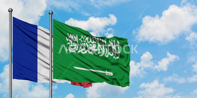 يرفرف علم فرنسا والسعودية معاً في مهب الريح أمام سماء زرقاء صافية تتلألأ فيها الغيوم البيضاء. مفهوم الدبلوماسية، العلاقات الدولية.