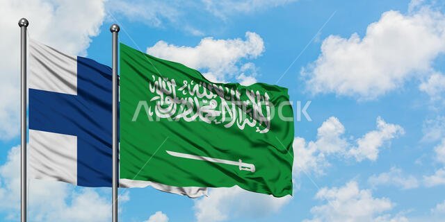 يرفرف علم فنلندا والسعودية معاً في مهب الريح أمام سماء زرقاء صافية تتلألأ بالغيوم البيضاء. مفهوم الدبلوماسية، العلاقات الدولية.