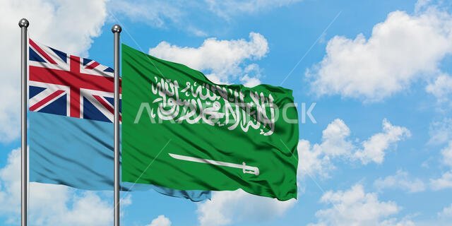 يرفرف علم فيجي وعلم المملكة العربية السعودية معاً في مهب الريح أمام سماء زرقاء صافية تتخللها غيوم بيضاء. مفهوم الدبلوماسية، العلاقات الدولية.