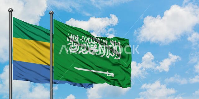 يرفرف علم الغابون وعلم المملكة العربية السعودية معاً في مهب الريح أمام سماء زرقاء ملبدة بالغيوم البيضاء. مفهوم الدبلوماسية، العلاقات الدولية.