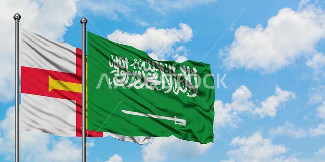 يرفرف علم غيرنسي وعلم المملكة العربية السعودية معاً في مهب الريح أمام سماء زرقاء ملبدة بالغيوم البيضاء. مفهوم الدبلوماسية، العلاقات الدولية.