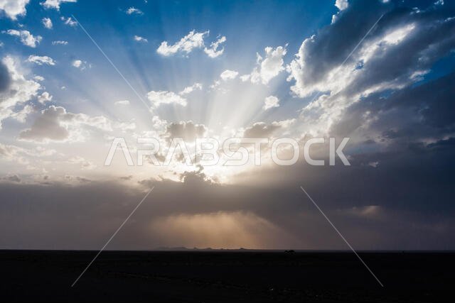 Sun rays beam through the thunderclouds over the desert in Saudi Arabia