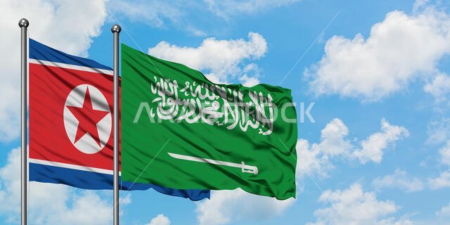 يرفرف علم كوريا الشمالية وعلم السعودية معاً في مهب الريح أمام سماء زرقاء ملبدة بالغيوم البيضاء. مفهوم الدبلوماسية، العلاقات الدولية.