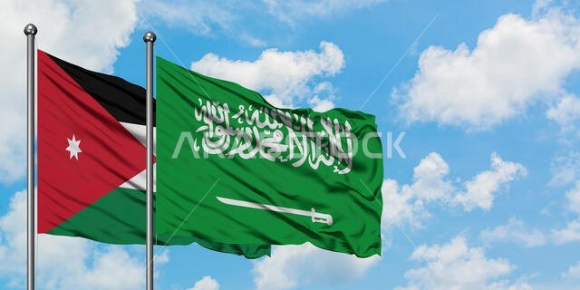 يرفرف علما الأردن والسعودية معاً في مهب الريح أمام سماء زرقاء صافية تتلألأ فيها الغيوم البيضاء. مفهوم الدبلوماسية، العلاقات الدولية.