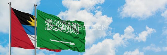 أنتيغوا وبربودا مع علم المملكة العربية السعودية يرفرف في مهب الريح أمام سماء زرقاء ملبدة بالغيوم البيضاء. مفهوم دبلوماسي، علاقات دولية.