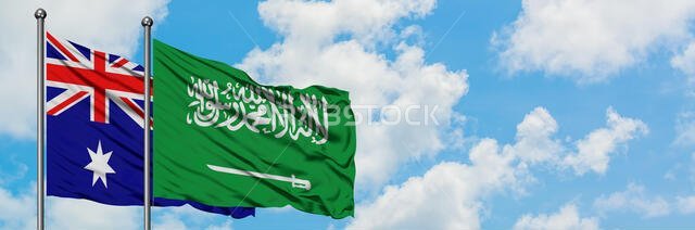 يرفرف علم أستراليا والسعودية معاً في مهب الريح أمام سماء زرقاء صافية تتلألأ فيها الغيوم البيضاء. مفهوم الدبلوماسية، العلاقات الدولية.